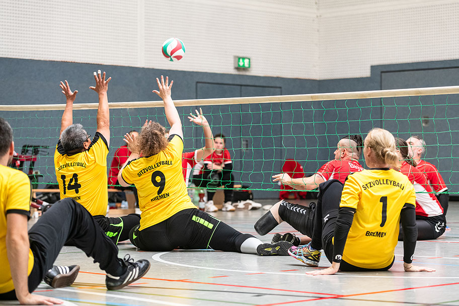 Zwei Mannschaften spielen Sitzvolleyball in der Halle.