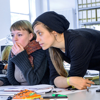 Zwei junge Frauen am Schreibtisch schauen auf einen Monitor.