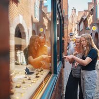 Mutter und Tochter stehen vor einem Schaufenster und zeigen auf die Auslage.