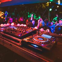 Ein DJ Pult und eine davor tanzende Menge. Bunte Lichter.