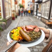 Eine Person hält eine Grünkohlpfanne im Schnoor in die Luft.