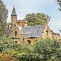 Das Wätjens-Schloss vom Weiten und eingebettet von Bäumen und Büschen.
