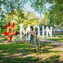 Das Foto zeigt eine Mutter mit ihren Kindern vor den Moin-Buchstaben in Bremen.