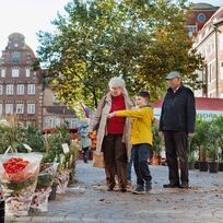 Großeltern gehen mit ihrem Enkel über einen Wochenmarkt.