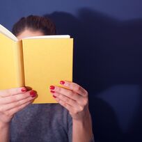 Eine Frau hält ein Buch vor ihr Gesicht.