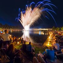 Menschen sitzen um den Hollersee und beobachten das Feuerwerk über dem See