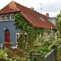 Ein blaues Wohnhaus mit rot-braunen Ziegeln, umgeben von Garten.