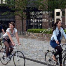 Junge Menschen auf fahren Fahrrad. Hinter ihnen Häuser und der Schriftzug "Willkommen in Bremen"