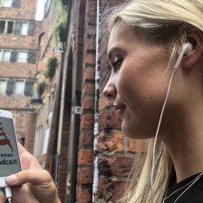 Eine junge Frau hält ihr Smartphone in der Hand. Auf dem Bildschirm ist das Logo des Bremen-Podcasts zu sehen.