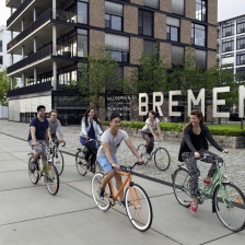 Eine Gruppe junger Leute fährt mit dem Fahrrad an dem Wort Bremen vorbei.
