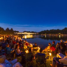 Viele Menschen sitzen um den Hollersee und genießen ein klassisches Konzert