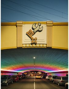 Das Foto bildet die Frontseite des Tunnels zum Stern hin ab inklusive Taube-Schlüssel Emblem bei Nacht. Der Tunnel wird in Regenbogenfarben erstrahlt.
