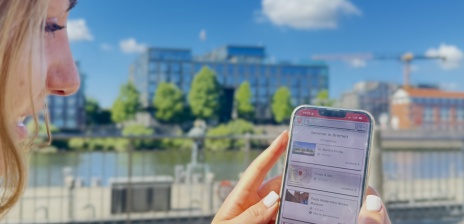 Someone is sitting by the Weser river with their cell phone, looking at the list of events for “Summer in Bremen” on the DBR app.
