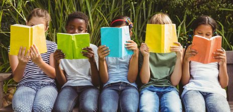 5 Kinder die lesend auf einer Bank im Grünen sitzen