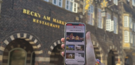 Jemand hält ein Handy mit der DBG App "Leben in Bremen" vor dem Beck´s Haus in Bremen 