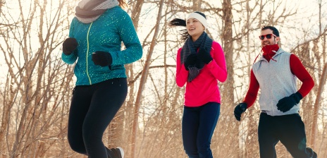 Drei Menschen in Sportkleidung und Handschuhen joggen durch den Wald.