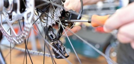 Nahaufnahme einer Speiche eines Fahrrads, dass mit einem Schraubenzieher repariert wird.