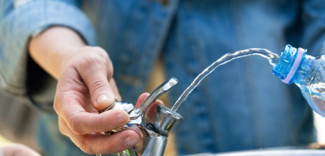 Jemand füllt Wasser an einem Trinkwasserbrunnen in eine Flasche.