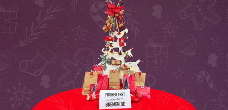 Ein festliches Bild mit einem Weihnachtsbaum mit den Bremer Stadtmusikanten, der mit kleinen Geschenkpaketen und roten Schleifen geschmückt sind. Unter dem Baum befinden sich Papiertüten und Geschenkverpackungen in Rot und Braun, die als Adventskalender mit Zahlen beschriftet sind. Ein Schild vor dem Arrangement trägt die Aufschrift „Frohes Fest wünscht Bremen.de“. Der Hintergrund ist lila mit weihnachtlichen Symbolen wie Schneeflocken, Sternen und Geschenkboxen.