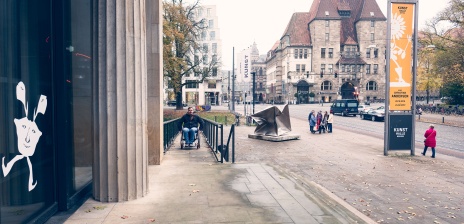 Ein Mann im Rollstuhl fährt die Rampe vor der Kunsthalle Bremen herauf.