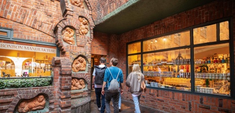 Vier Personen laufen in der Böttcherstraße an der Bonbonmanufaktur und dem Sieben-Faulen-Brunnen vorbei.