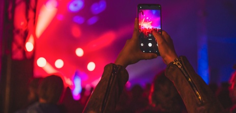 Person taking a photo of a concert scene illuminated by vibrant red and blue lights.
