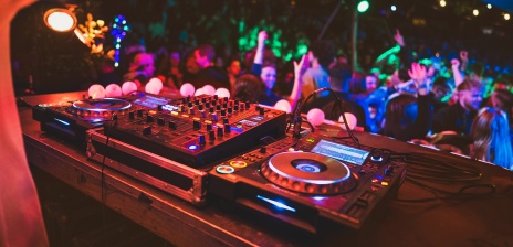 Ein DJ Pult und eine davor tanzende Menge. Bunte Lichter.