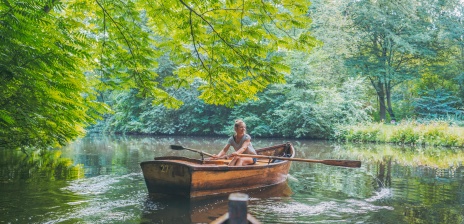 Eine Frau fährt mit einem Ruderboot durch ein Waldstück
