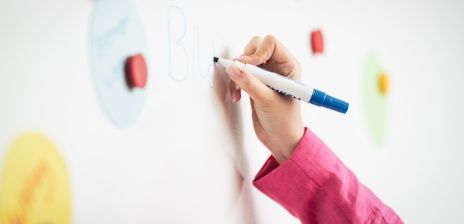 Eine Frauenhand schreibt auf ein Whiteboard das Wort Bildung