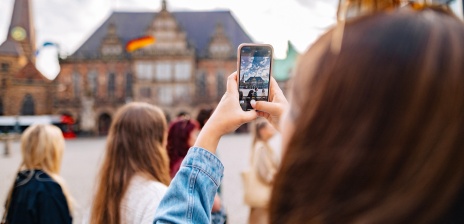 Eine Person steht am Marktplatz und macht mit dem Handy ein Foto vom Rathaus.