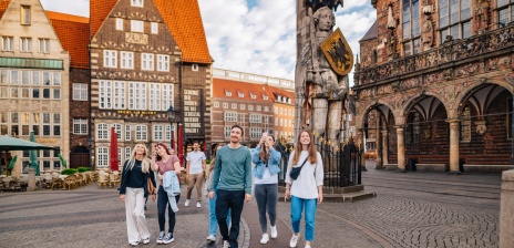 Eine Gruppe jüngerer Menschen besichtigt den Bremer Marktplatz mit Rathaus und Roland