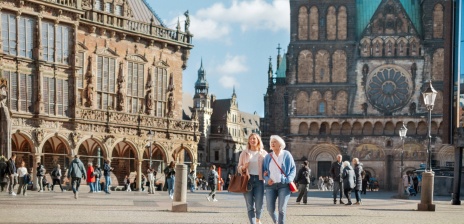 Zwei Damen laufen über einen großen Platz und eine Kirche ist im Hintergrund.