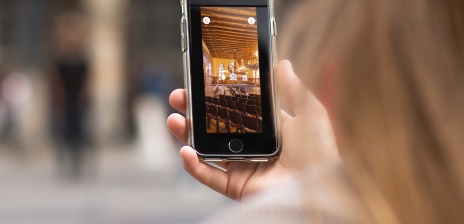 Eine Frau hält ein Smartphone in der Hand. Darauf sieht sie ein Bild vom Inneren des Bremer Rathauses. 