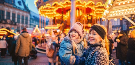 Eine Frau hat ein Mädchen auf dem Arm, sie steht vor einem Karussell auf dem Bremer Weihnachtsmarkt.