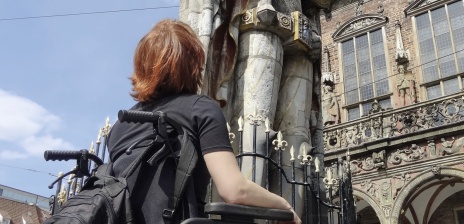 Eine Person sitzt in einem Rollstuhl und guckt sich eine steinerne Statue an. 