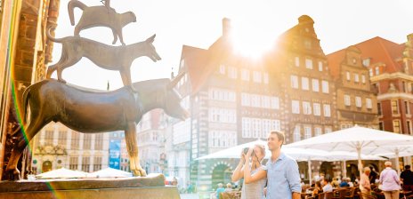 Eine Frau und ein Mann stehen vor den Bremer Stadtmusikanten. Die Frau macht von der Bronzestatue ein Bild.