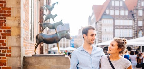 Eine Frau und ein Mann stehen vor den Bremer Stadtmusikanten. 