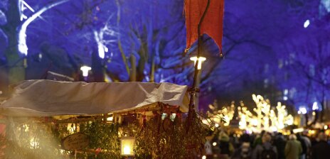 Im Vordergrund sieht man einen alten Wagen auf dem Schlachte Zauber, an dem Mistelzweige hängen. Im Hintergrund laufen Menschen über die Schlachte, welche winterlich geschmückt und beleuchtet ist. 