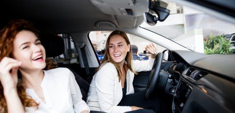 Zwei junge Frauen sitzen gemeinsam im Auto und lachen.