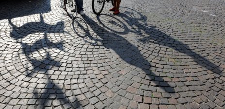 Zwei Personen schieben ihre Fahrräder an den Stadtmusikanten vorbei. Ihre Schatten sind zu sehen.