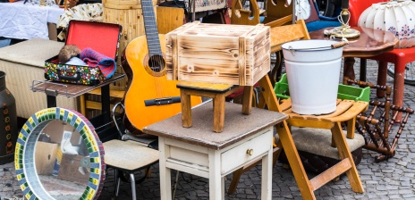 Eine Flohmarktszene von einem Stand mit kleinen Möbeln wie Nachtschränken und einer Gitarre.