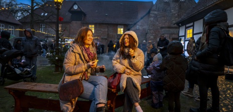 Zwei Frauen sitzen mit einem Glühwein an einer Feuerstelle.