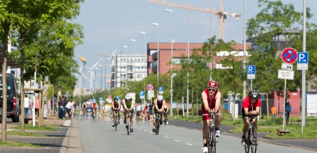 Triathlon-Teilnehmer fahren auf Fahrrädern über die Straße.