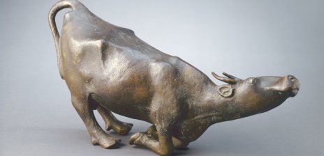 Eine Skulptur einer Kuh. Sie kniet sich nieder und erhebt ihren Kopf. 