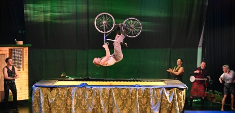 Ein Mann macht mit einem Fahrrad auf einer Bühne Akrobatik.