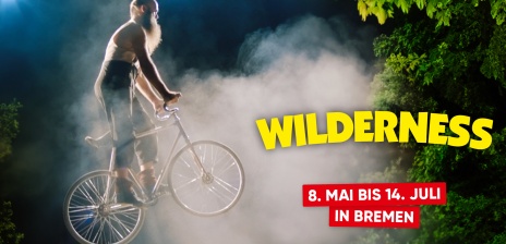Ein Bild, auf dem ein bärtiger Fahrradfahrer vor Rauch und Gebüsch in die Höhe springt. Daneben Steht: Wilderness: 8. Mai bis 14. Juli in Bremen.