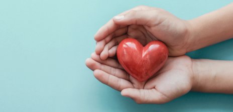 Zwei Hände halten ein kleines rotes Herz aus Stein.