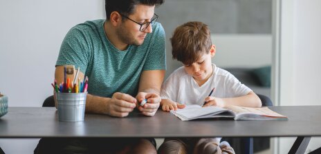 Ein Mann und ein Junge sitzen am Tisch und machen gemeinsam Hausaufgaben.