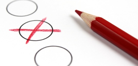 Ein roter Buntstift neben einem mit Kreuz markierten Kreis