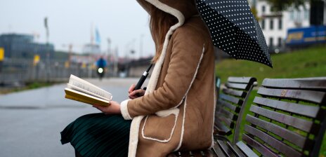 Eine Frau sitzt auf einer Bank am Osterdeich und liest.
